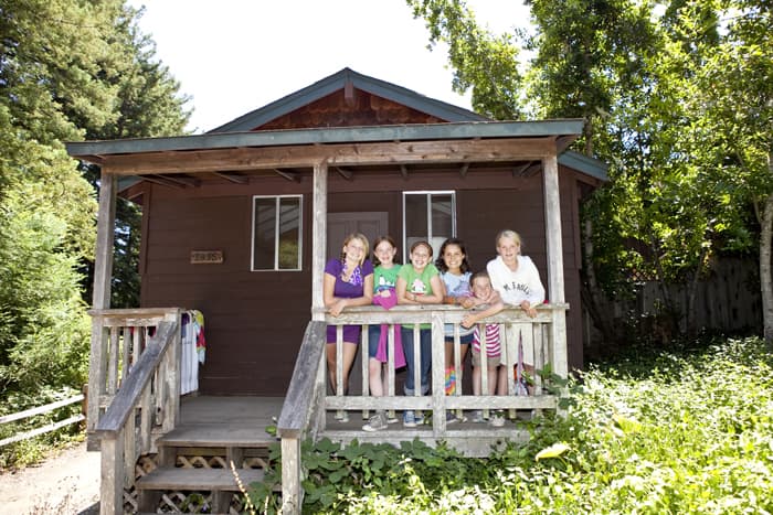 Six girls in front of a cabin smiling