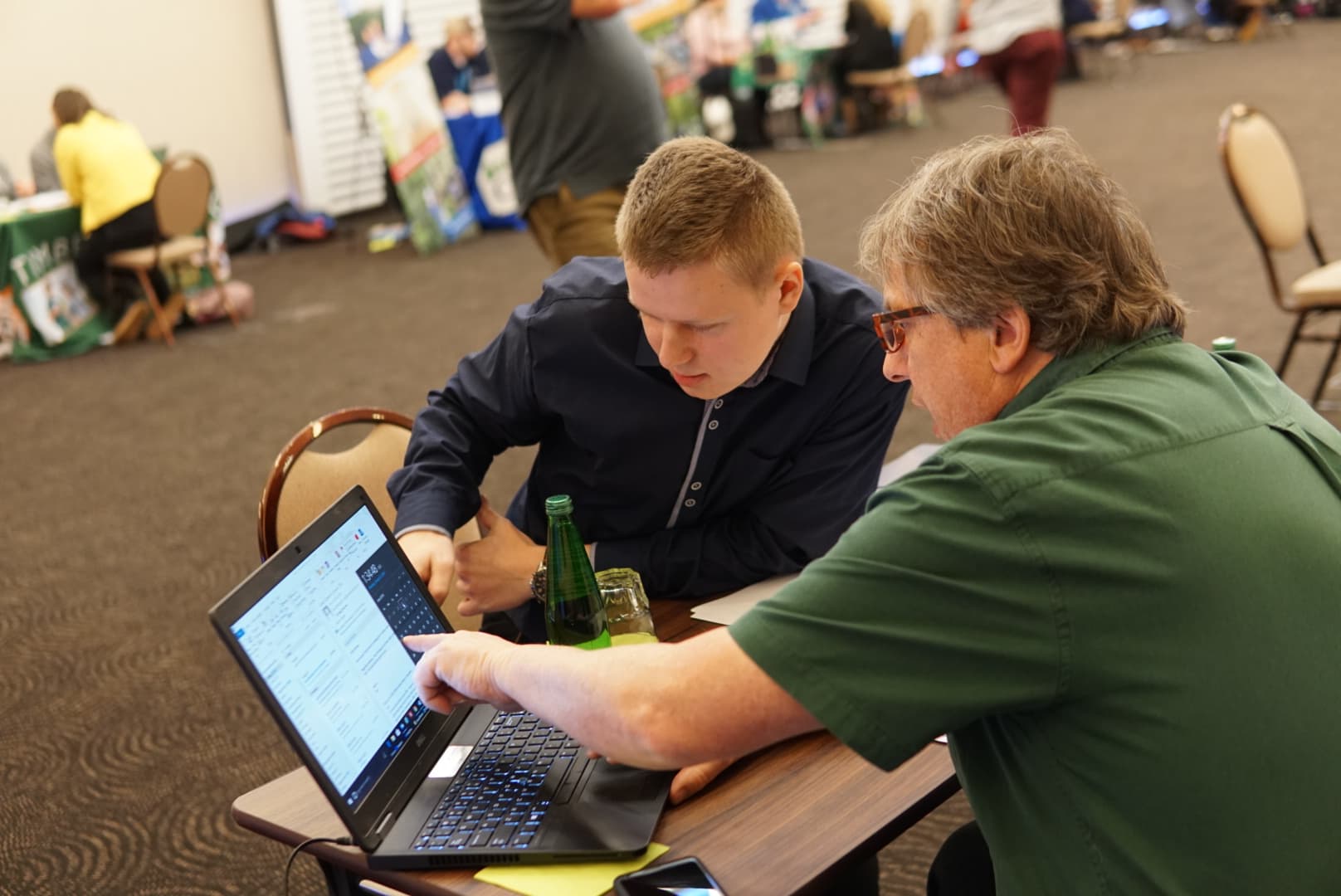 A boy looks on as a representative explains things on a computer