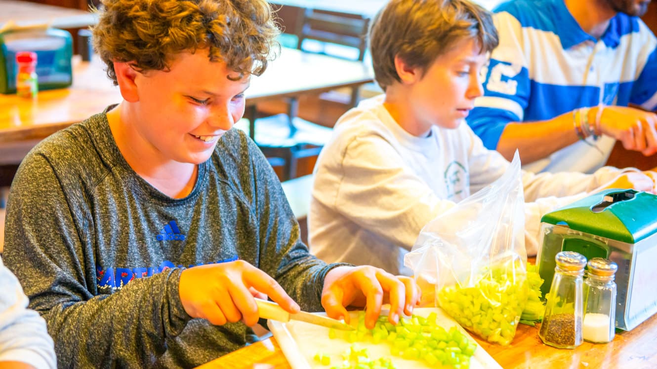 Boy slices celery during summer camp culinary arts