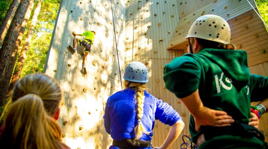 Camper climbs rock wall while other watch