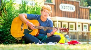 camper plays guitar while sitting on grass