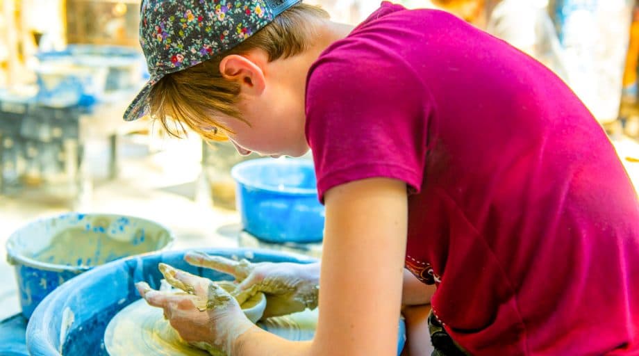 Camper leans over pottery wheel