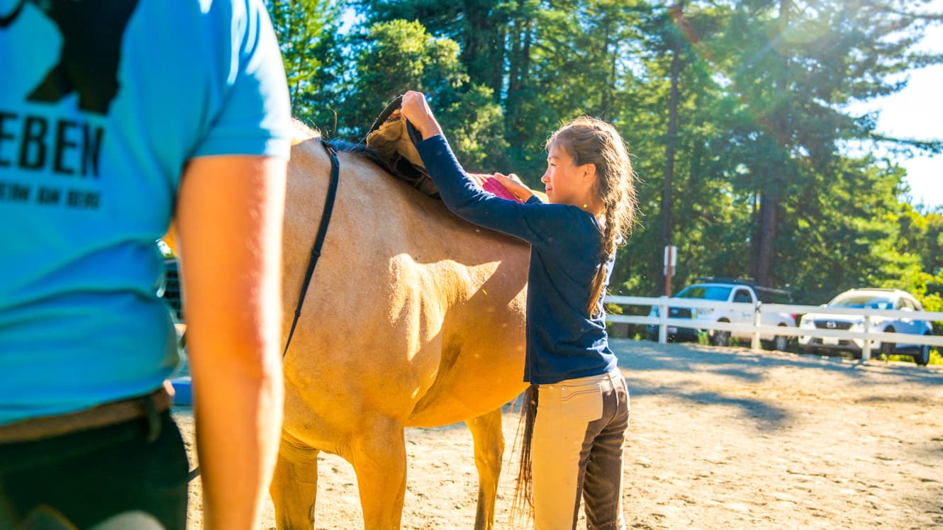 Girl put saddle on horse at summer camp