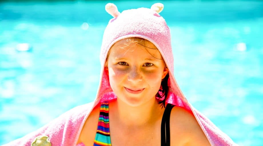 Camper sits by pool with pink towel over head