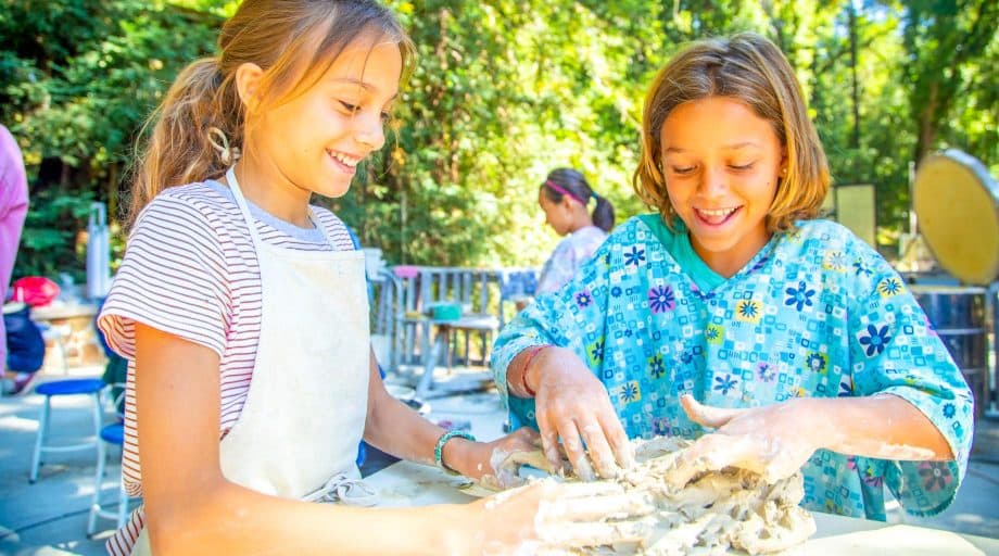 Two girls work with wet clay at summer camp