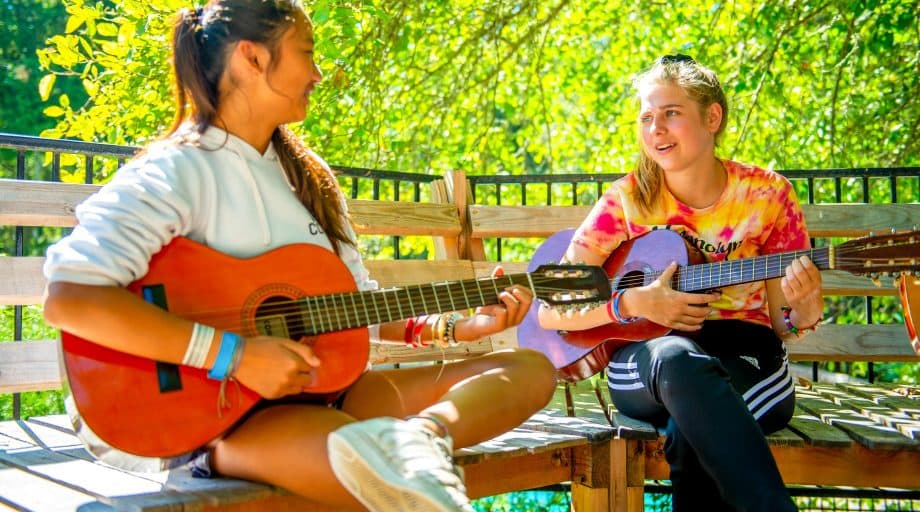 Two girls play guitars at summer camp