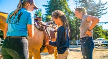 Camper and counselors tend to horse's saddle