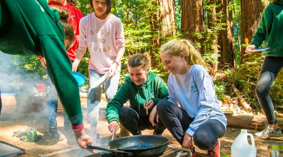 Campers gather around outdoor cooking pan