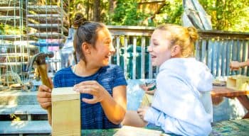 Two girls laughing and talking while building bird houses