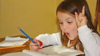 A little girl makes a funny face while doing homework