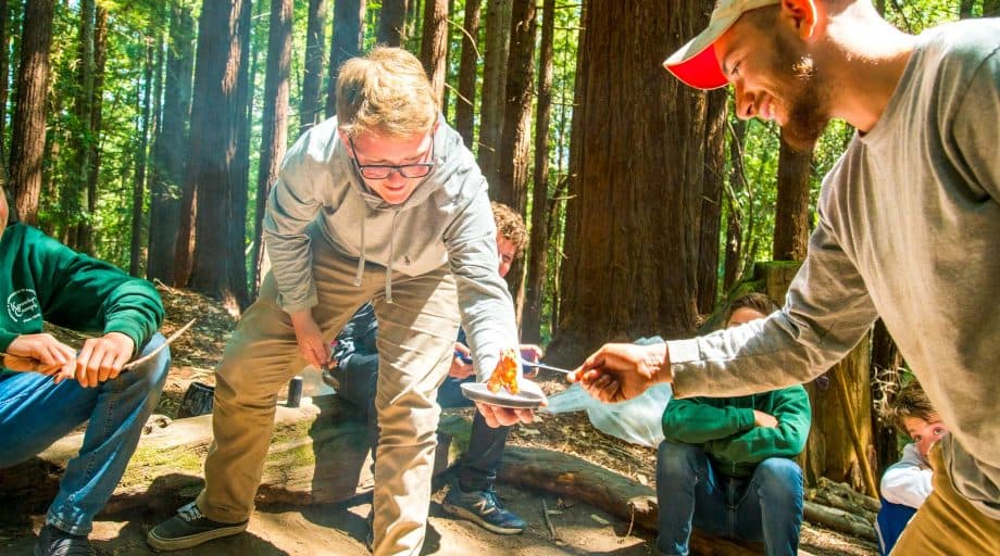 Counselor gives camper bacon from outdoor cooking