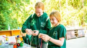 Girls making friendship bracelets outside