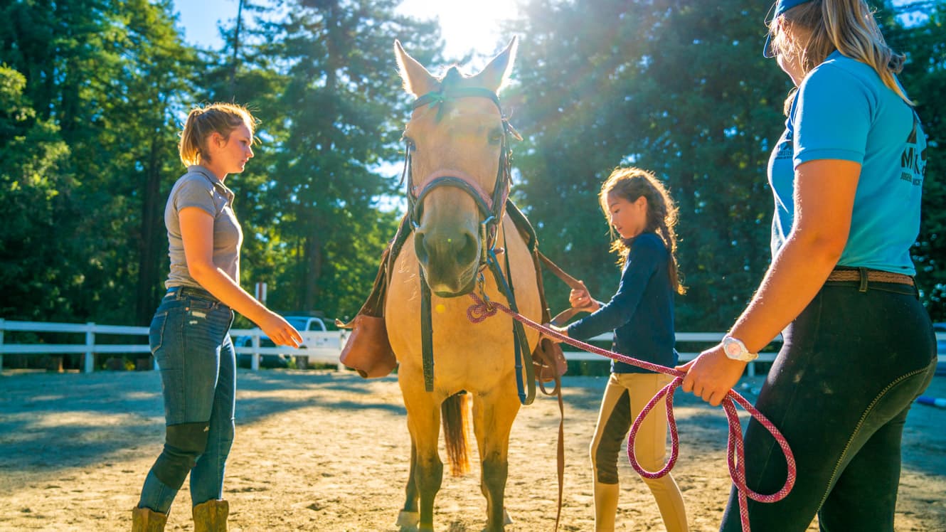 Camper and staff prepare horse for riding