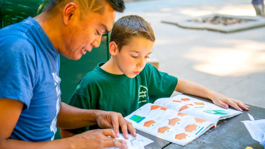 Staff member helps camper do origami