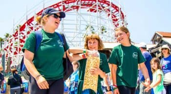 A counselor and two campers walk around the boardwalk with popcorn