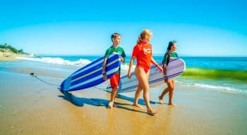 Counselor and campers walk down beach with surfboards