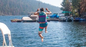 A camper in a life vest jumps off the dock into the lake