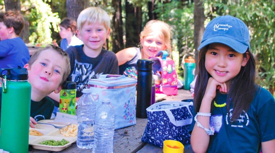 Campers at a picnic table eating lunch and smiling