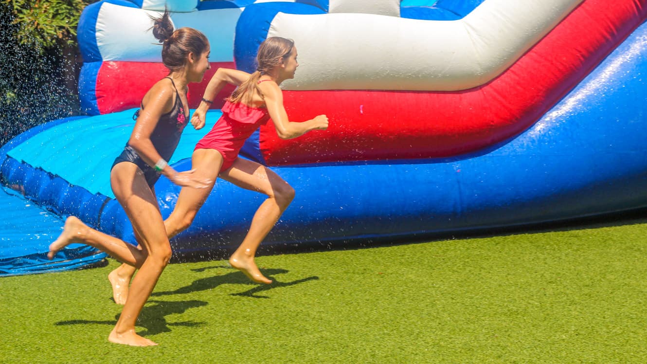 Girls running on grass next to inflatable waterslide