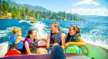 Four kids on a boat with a tube behind them