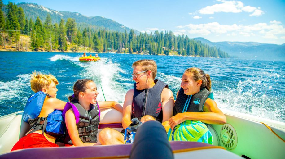 Four kids on a boat with a tube behind them